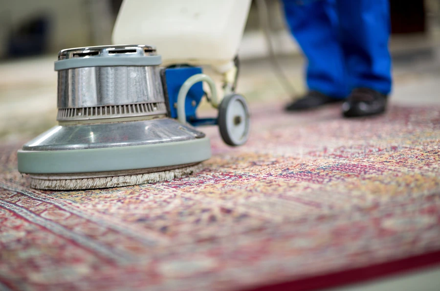 ground view of a round carpet vacuum with blurry background of carpet cleaner guy with blue pants