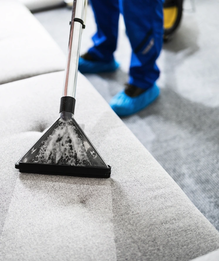 upholstery cleaning guy wearing blue pants and blue shoes using a vacuum to clean sofa