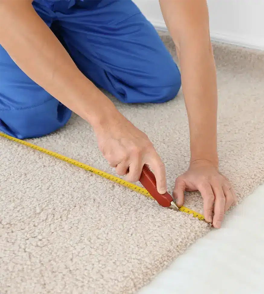 carpet repairman wearing blue pants holding a measuring tape and cutting a carpet into size