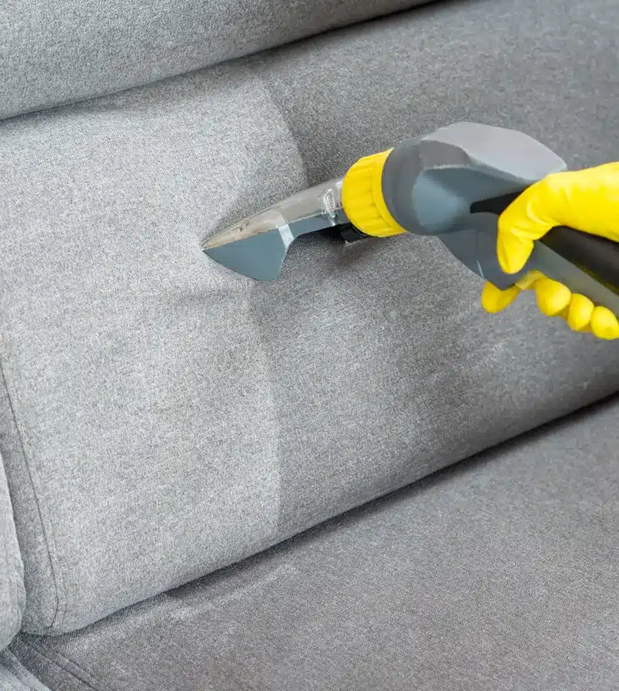 right hand wearing yellow glove holding a vacuum cleaning a couch