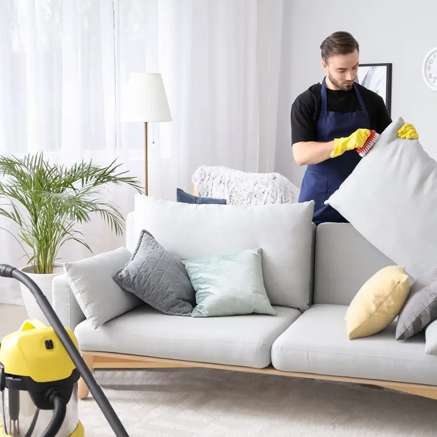 Upholstery guy wearing black shirt and blue cleaning apron brushing a pillow