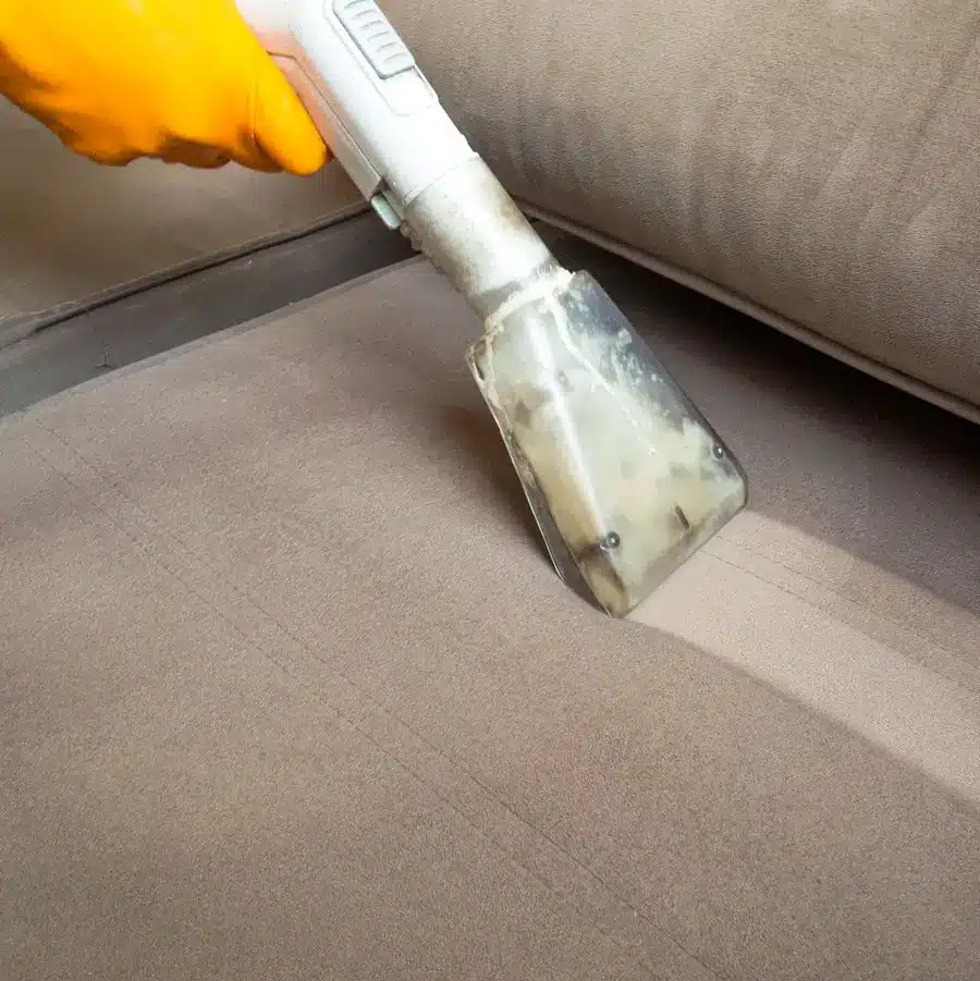 a hand with a yellow glove cleaning a dirty couch with vacuum.
